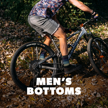 a person riding a mountain bike in a forest setting with the promotional text 'Men's Bottoms' overlayed