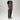 A man wearing dark gray bib overalls over a black t-shirt and black sneakers, standing against a light gray studio background.