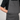A close-up of a person wearing dark gray canvas bib overalls over a black t-shirt, showing the front chest pocket with a snap button and the brand name 'JAPAN' embroidered on the chest.