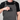 A close-up of a person wearing dark gray work overalls over a black t-shirt, demonstrating a black textured wallet or phone case tucked into the front utility pocket.
