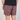 A person wearing multicolor patterned swim trunks with a black t-shirt, shown from the waist down against a light gray studio background.