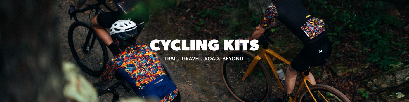A dark promotional banner for cycling kits, featuring two cyclists on bicycles in a forest setting with the text 'CYCLING KITS' and 'TRAIL, GRAVEL, ROAD. BEYOND.