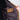 Close-up of a person holding open a quilted jacket to show the interior lining, featuring a brown corduroy pocket and trim with dark buttons, against a light gray background.