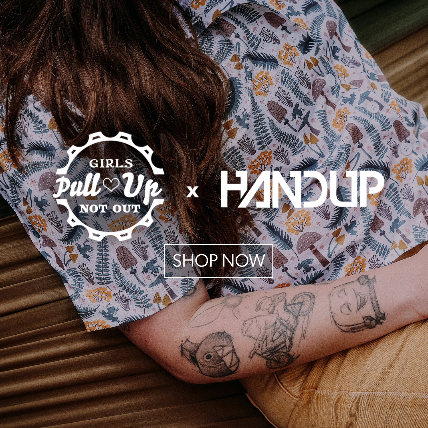 A person wearing a short-sleeve button-up shirt with a botanical and animal print in muted blue, green, brown, and yellow tones. The photo includes overlaid text reading 'Girls Pull Up Not Out' and 'x HANDUP' with a 'SHOP NOW' button.