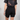 Person wearing black shorts and a black t-shirt with a tie, on a plain background