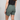 person wearing green shorts and a black shirt with a plain background