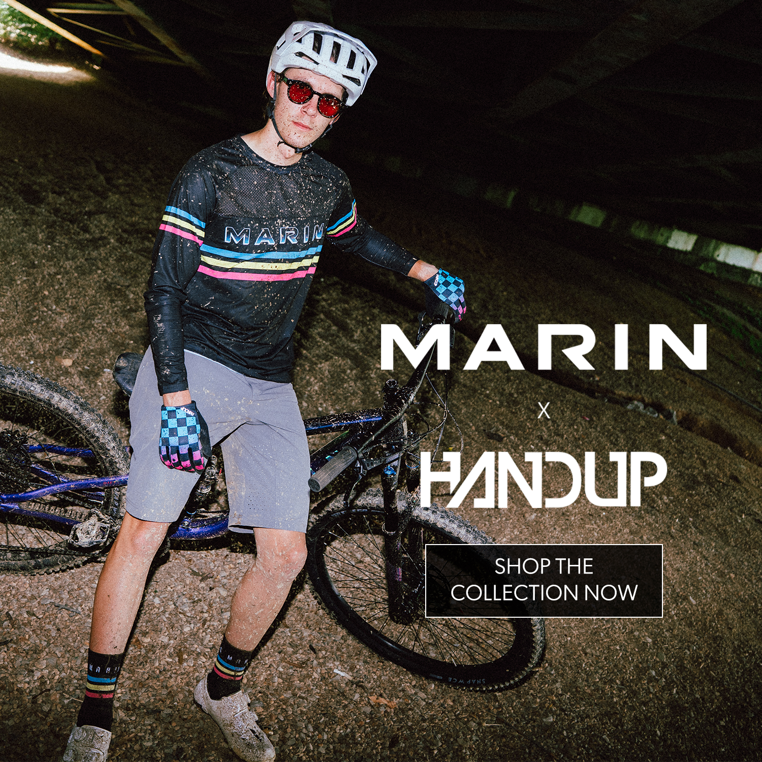 Person wearing cycling gear with a bicycle, standing in a tunnel, promoting Marin x Handup collection.