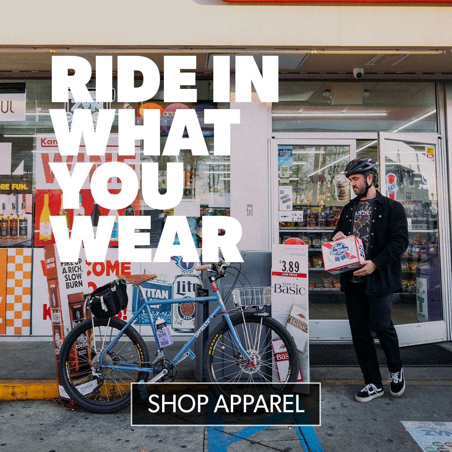 Man holding a box with text 'Ride in What You Wear' and 'Shop Apparel' displayed in front of a store.