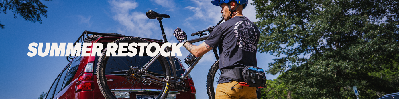 Person loading a bicycle into the back of a red car with 'Summer Restock' text overlay.