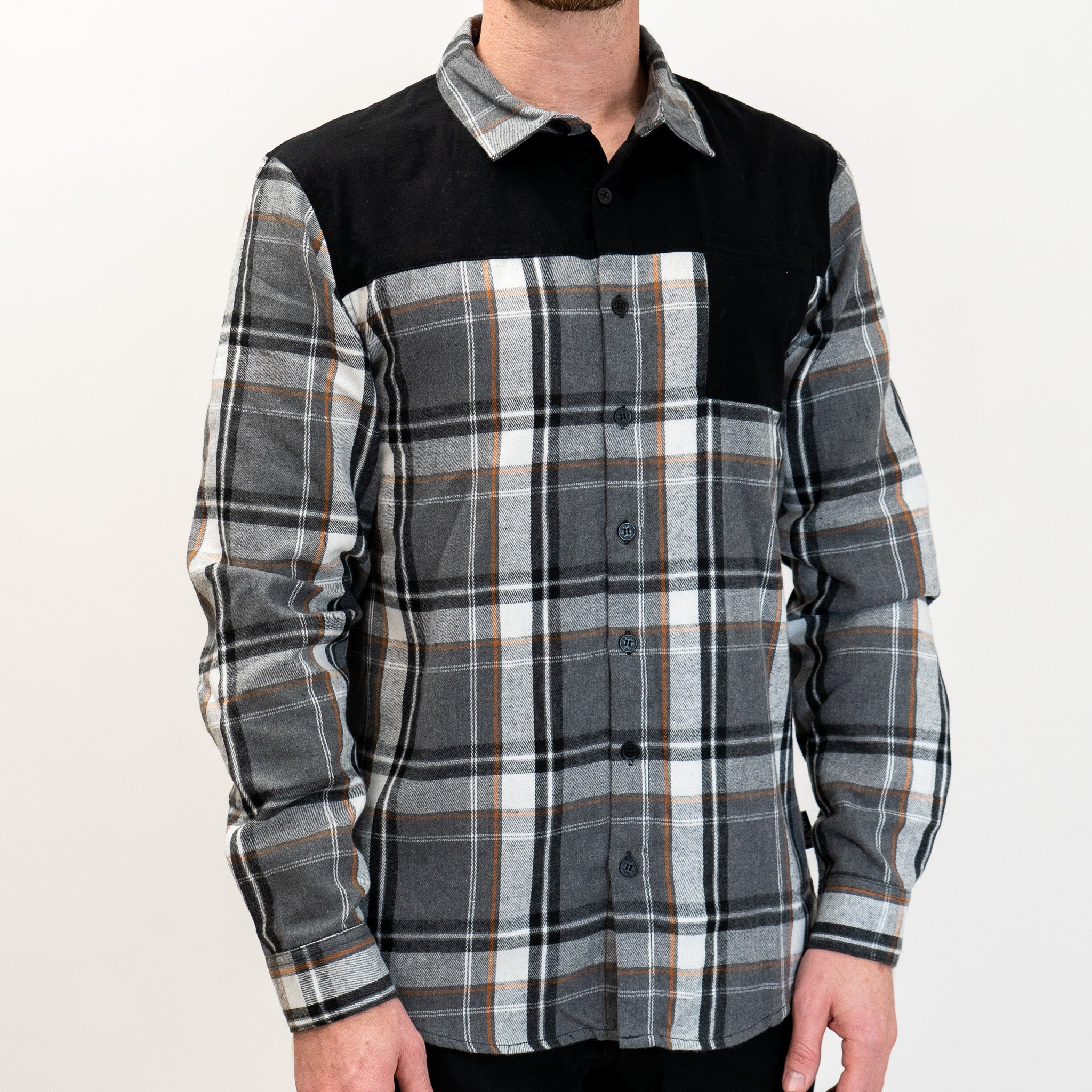 A long-sleeved Flannel Button Up shirt with a checkered pattern in black, gray, and white, featuring a solid black panel across the top shoulders.