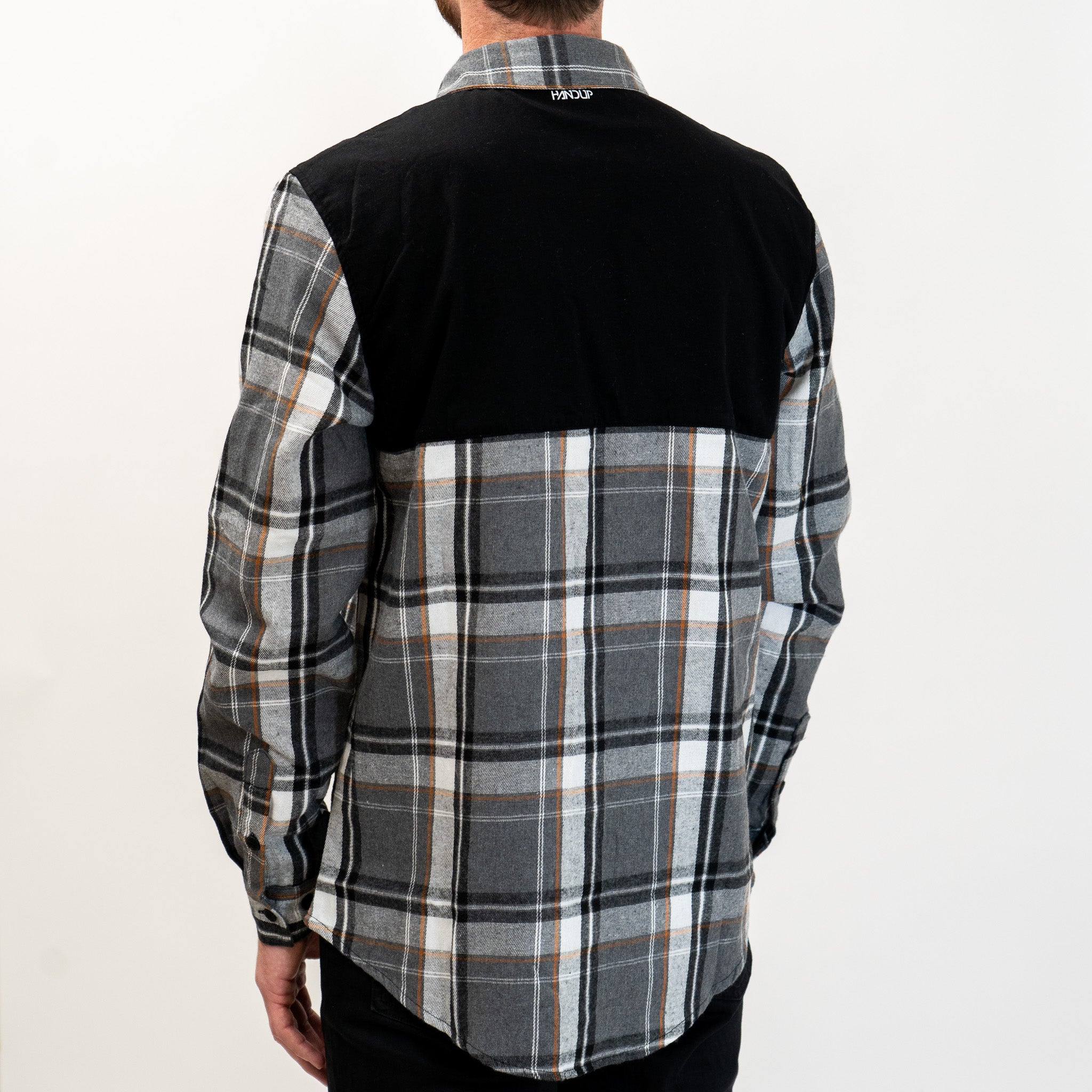 A long-sleeved Flannel Button Up shirt with a checkered pattern in black, gray, and white, featuring a solid black panel across the top shoulders.