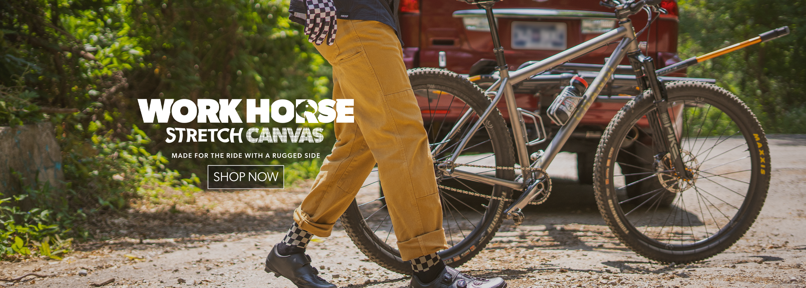 Person walking with a bicycle on a dirt road, featuring 'Work Horse Stretch Canvas' branding.
