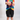 A child wearing a vibrant tie-dye t-shirt and black athletic shorts, pointing forward with both hands against a light gray studio background.