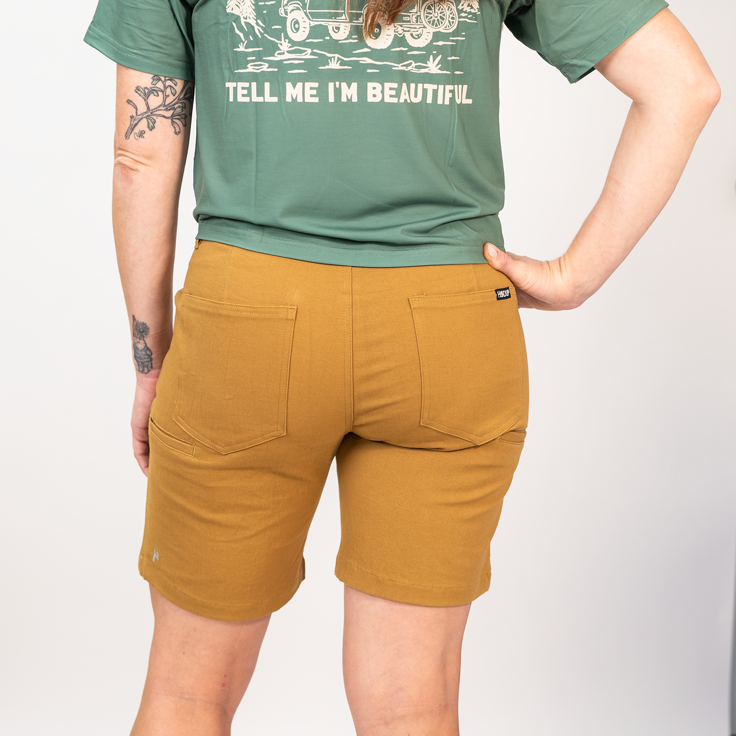 Person wearing a green t-shirt with text and brown shorts on a white background