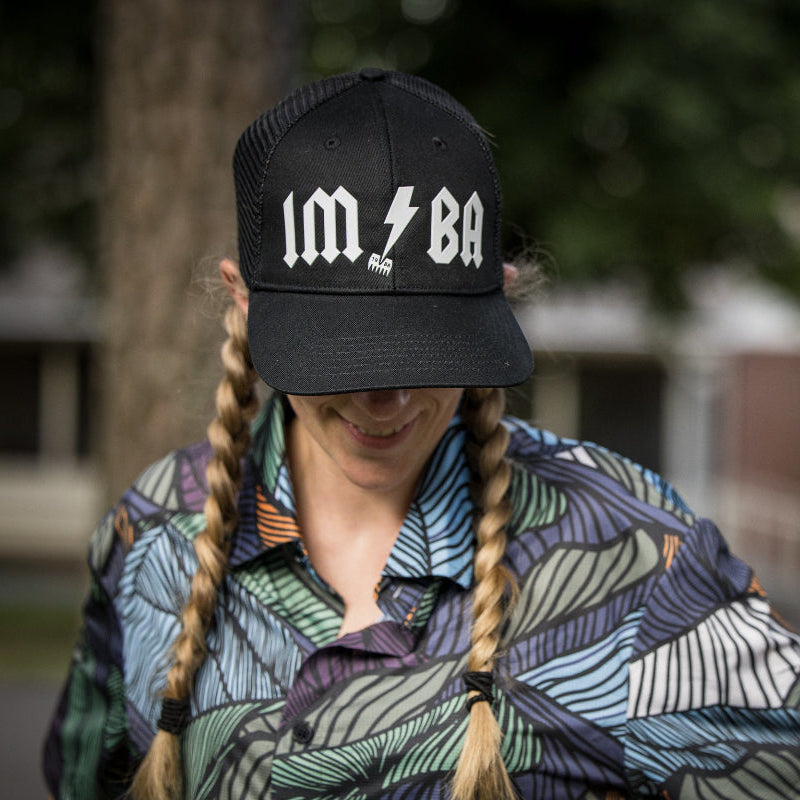Person wearing a black cap with 'IMBA' logo, smiling outdoors.