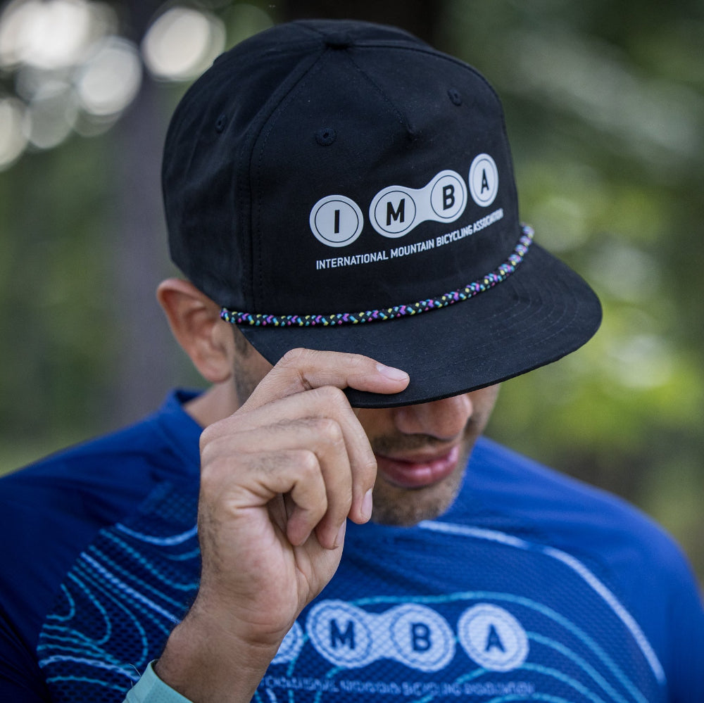 Person wearing a black cap and blue shirt with 'IMBA' logo outdoors
