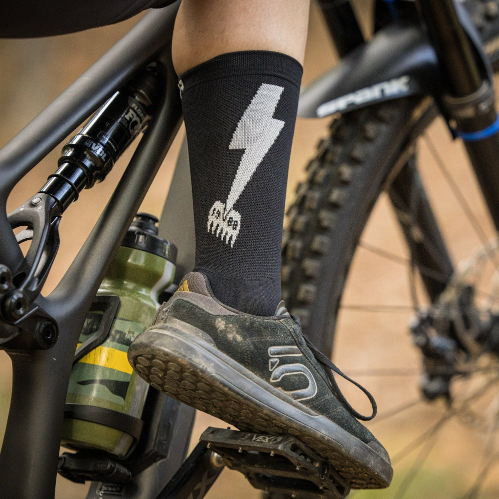 Person wearing black socks with a white logo on a mountain bike
