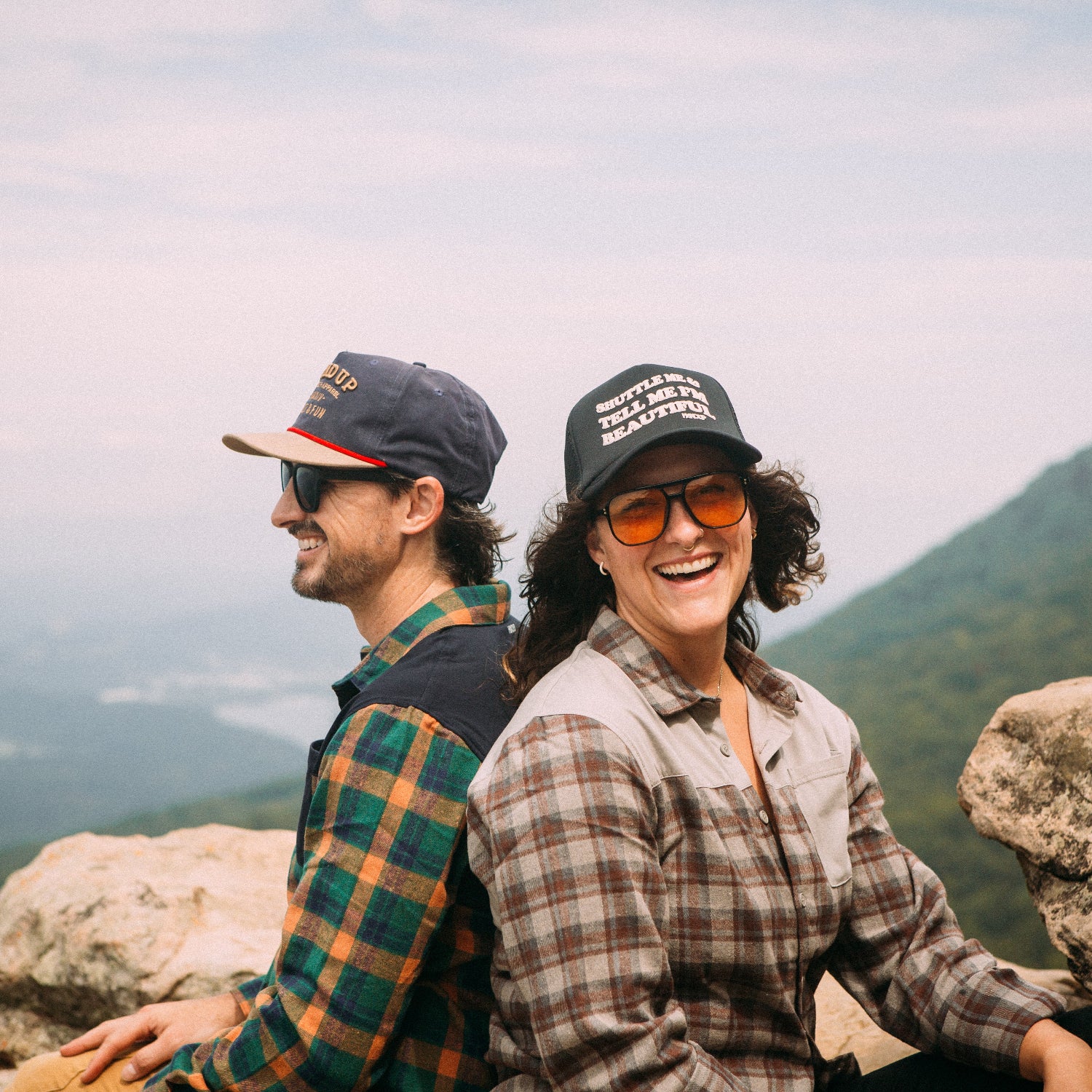 Two people sitting on a rocky outcrop with mountains in the background