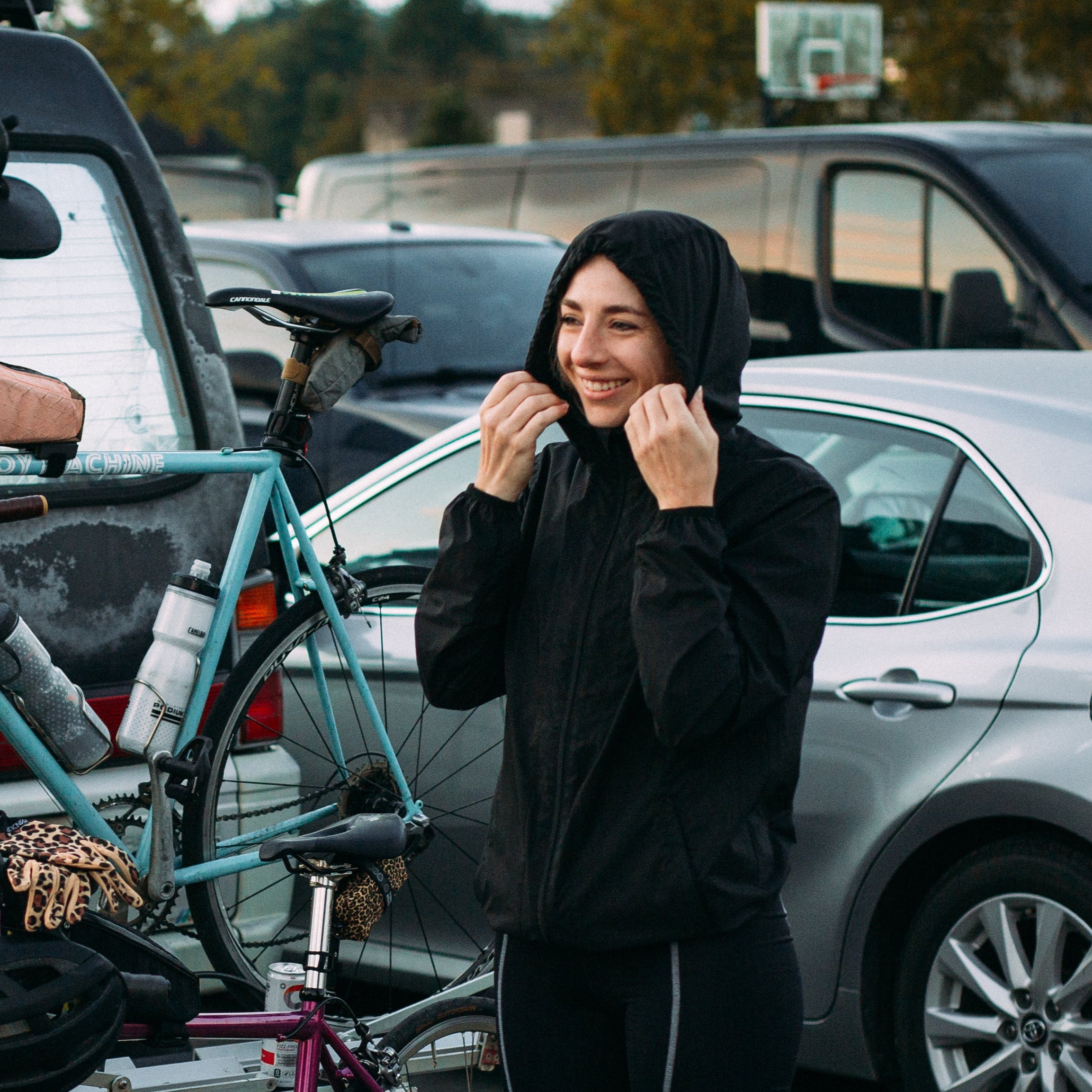 Person standing next to bicycles in a parking lot with cars and vans in the background