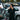 Person standing next to bicycles in a parking lot with cars and vans in the background