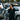 Person standing next to bicycles in a parking lot with cars and vans in the background