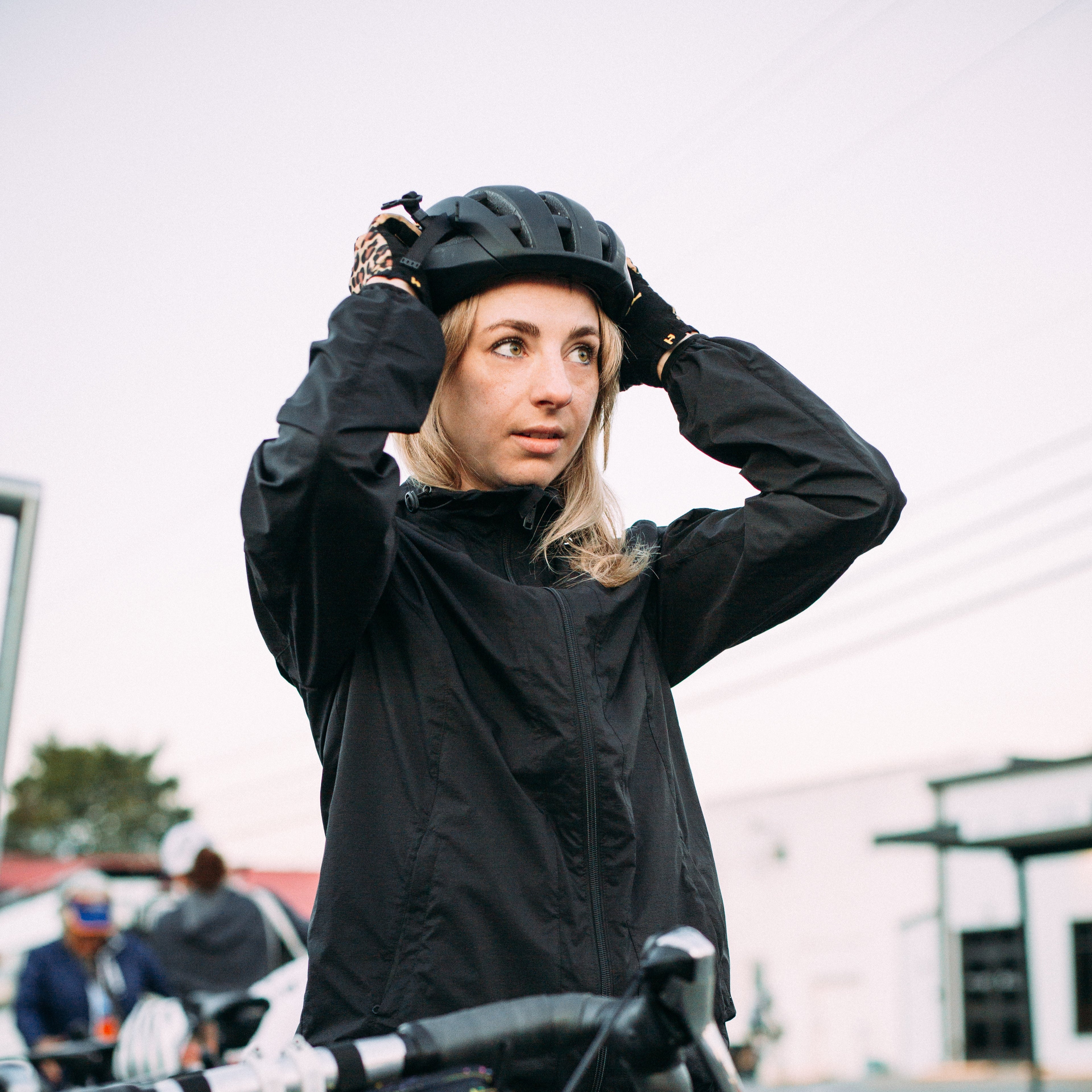Woman adjusting a helmet while standing next to a bicycle on a street.