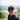 Man wearing a black cap with a logo and sunglasses, standing outdoors with a blurred natural background