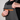 Close-up of a person wearing dark gray bib overalls over a black shirt, demonstrating a bright orange zipper pocket on the chest.