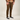 A person wearing slim-fit brown pants, a brown and orange plaid flannel shirt, and black low-top sneakers, photographed against a plain light beige studio background.
