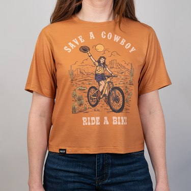 Person wearing a brown t-shirt with a graphic design and text on a plain background