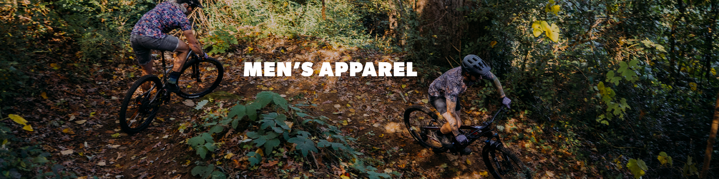 Two people mountain biking through a forest with 'Men's Apparel' text overlay.