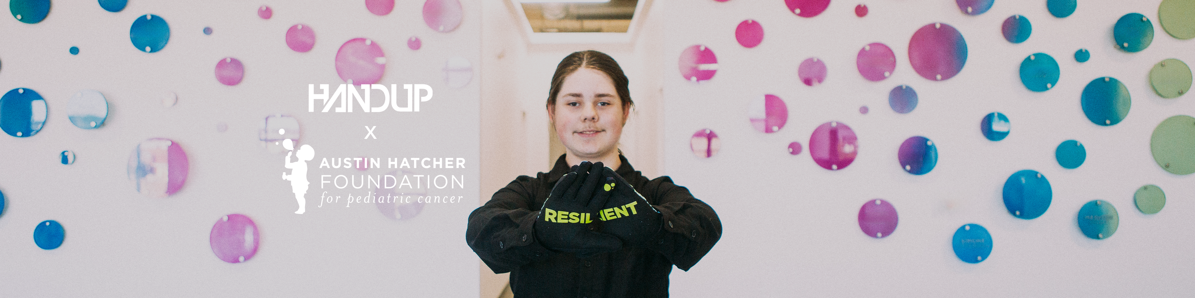 Person wearing a black hoodie with visible branding in front of a colorful polka dot wall.