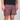 A close-up of a person wearing patterned athletic shorts and a black t-shirt against a light gray studio background. The shorts feature a dense multicolor abstract print with pink, yellow, blue, and black shapes.
