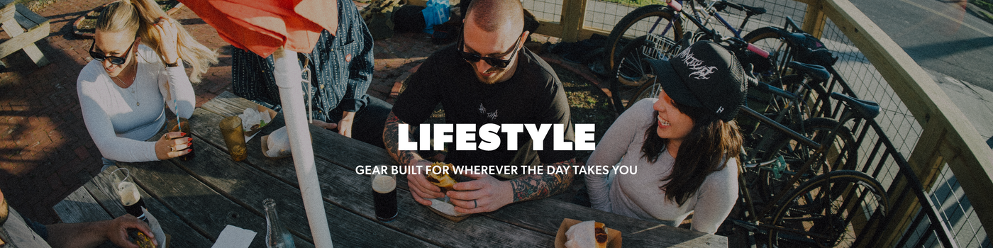 A lifestyle banner featuring three people sitting and cycling on an outdoor deck, with a central text overlay reading 'LIFESTYLE' and 'GEAR BUILT FOR WHEREVER THE DAY TAKES YOU'.