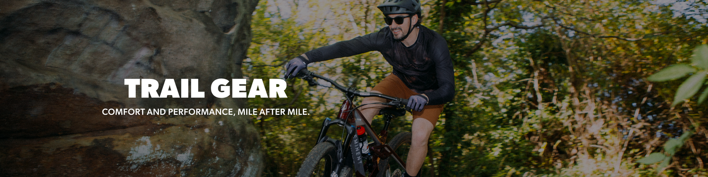 A mountain biker riding on a forest trail with the text 'TRAIL GEAR' and 'COMFORT AND PERFORMANCE, MILE AFTER MILE.' overlaid on the left side.