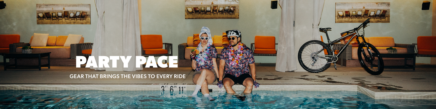 Two women wearing colorful patterned swim shirts sit in a pool next to a bicycle, with large text reading 'PARTY PACE' and smaller text 'GEAR THAT BRINGS THE VIBES TO EVERY RIDE' on a lounge poolside scene.