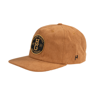 A tan corduroy baseball cap with a black and gold embroidered patch on the front reading 'Harder Gloves Co Apparel' and a small black embroidered 'H' logo on the side, shown against a plain white background.