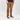 A person wearing brown corduroy pants, a black t-shirt, and black low-top sneakers with white laces and soles, standing against a light gray studio background.