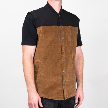 A man wearing a short-sleeve button-front shirt with a black collar and sleeves and a brown suede-like front panel, photographed against a light gray studio background.