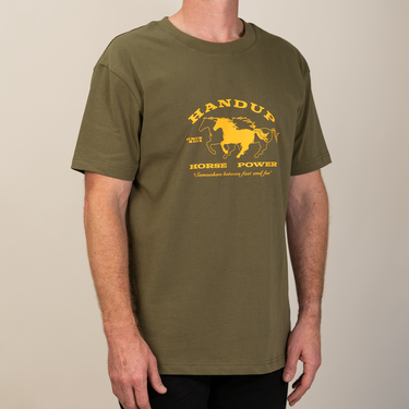 A man wearing an olive green t-shirt with a yellow graphic print on the chest that reads 'HANDUP HORSE POWER' with a horse illustration, photographed against a plain beige background.