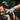 Close-up of a person's hand wearing a spotted glove on a bike handlebar with another person in the background.