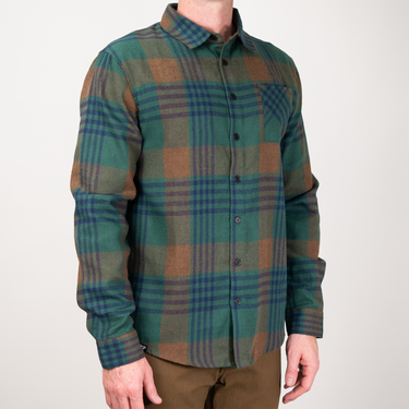 A man wearing a green and brown plaid button-down flannel shirt, shown from the neck down against a plain light gray background.