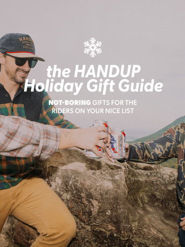 Two men sitting on a rock outdoors, with text overlay about the HANDUP Holiday Gift Guide.