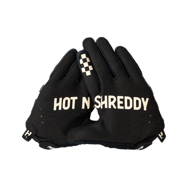 A pair of black motorcycle gloves with 'HOT N SHREDDY' printed in beige across the back of one glove, featuring a beige and black checkered pattern on the index finger of the other glove, set against a plain white background.