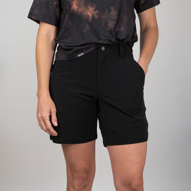 Person wearing black shorts and a black t-shirt with a tie, on a plain background