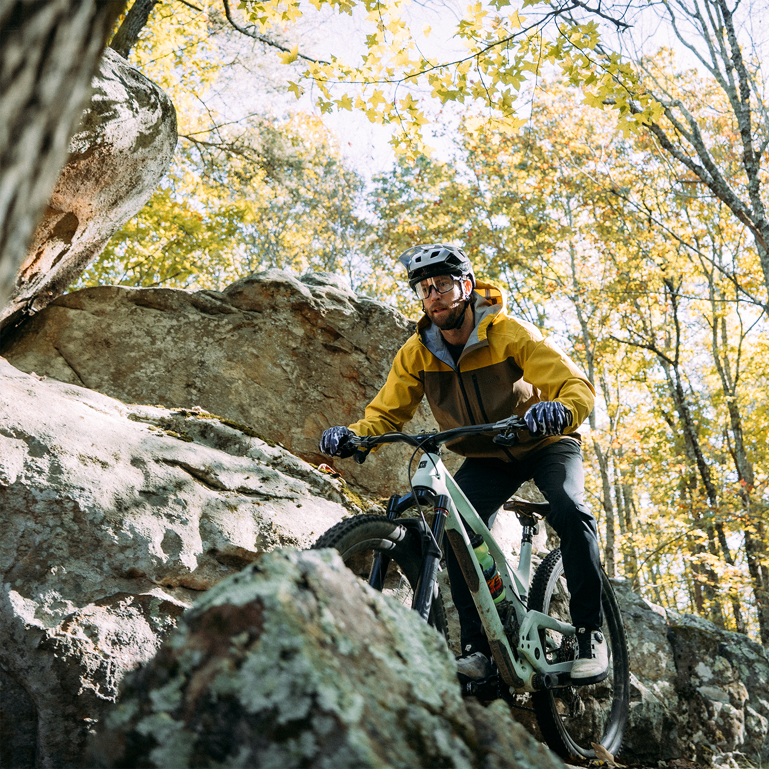 Person mountain biking through rocky terrain with autumn foliage