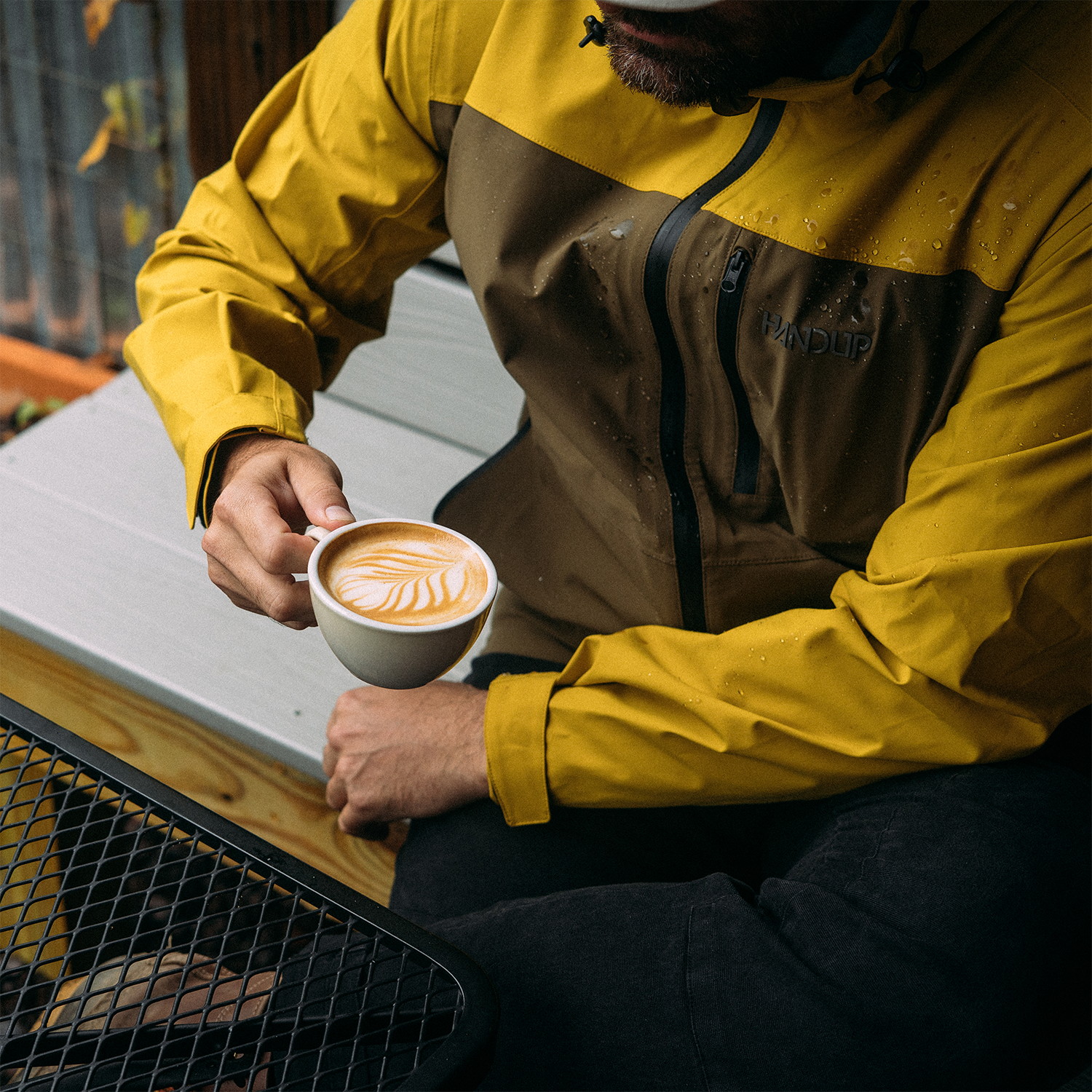 Person in a yellow raincoat holding a cup of coffee outdoors
