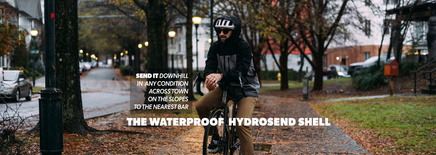 Person riding a bike on a city street with text about a waterproof hydrosend shell.