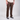 A person wearing brown straight-leg corduroy pants, a light beige t-shirt, and black canvas sneakers with white soles, standing against a light gray studio background.