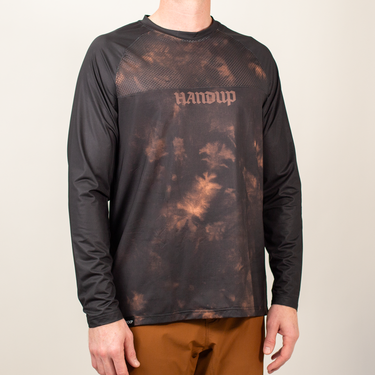 a person wearing a long sleeve mountain bike jersey with a black and tan tie dye design and 'HANDUP' logo